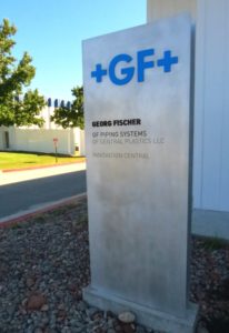 Picture of metal monolith type sign in front of building, silver with blue letters.